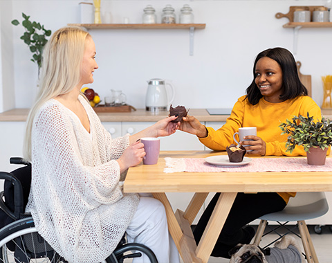 Two women, one in a wheelchair enjoy coffee together at a table, Presenting respite support